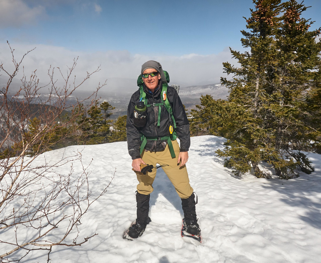 A hiker smiling atop a snow covered mountain 