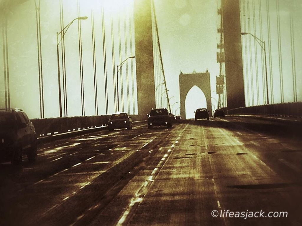 automobiles commute on a bridge cast in shadow of the sun overhead.