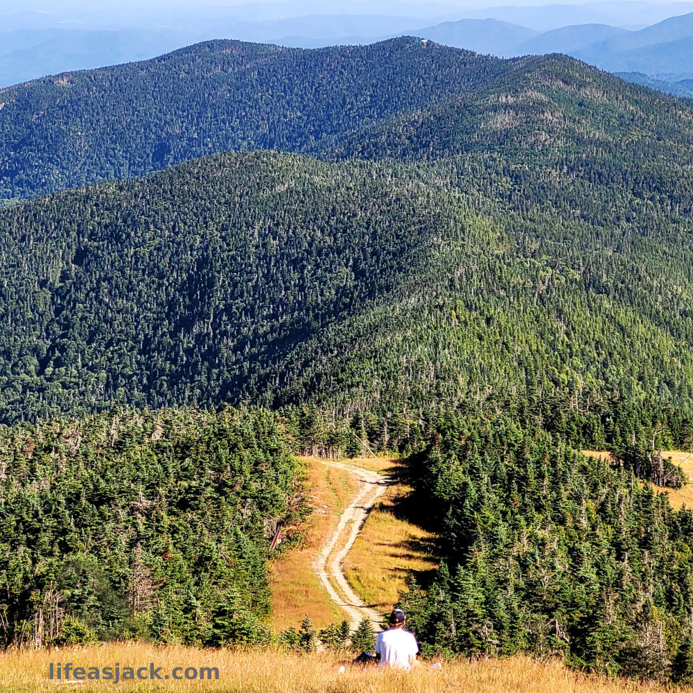 a solo hiker sits facing a range of mountains in Vermont.