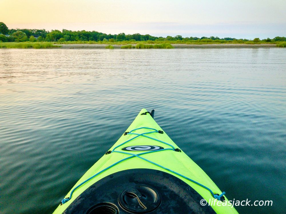a green kayak bow points towards a sandy shore
