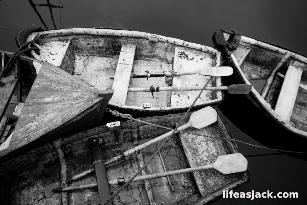 black and white image of skiffs secured to a dock by Galway Bay.