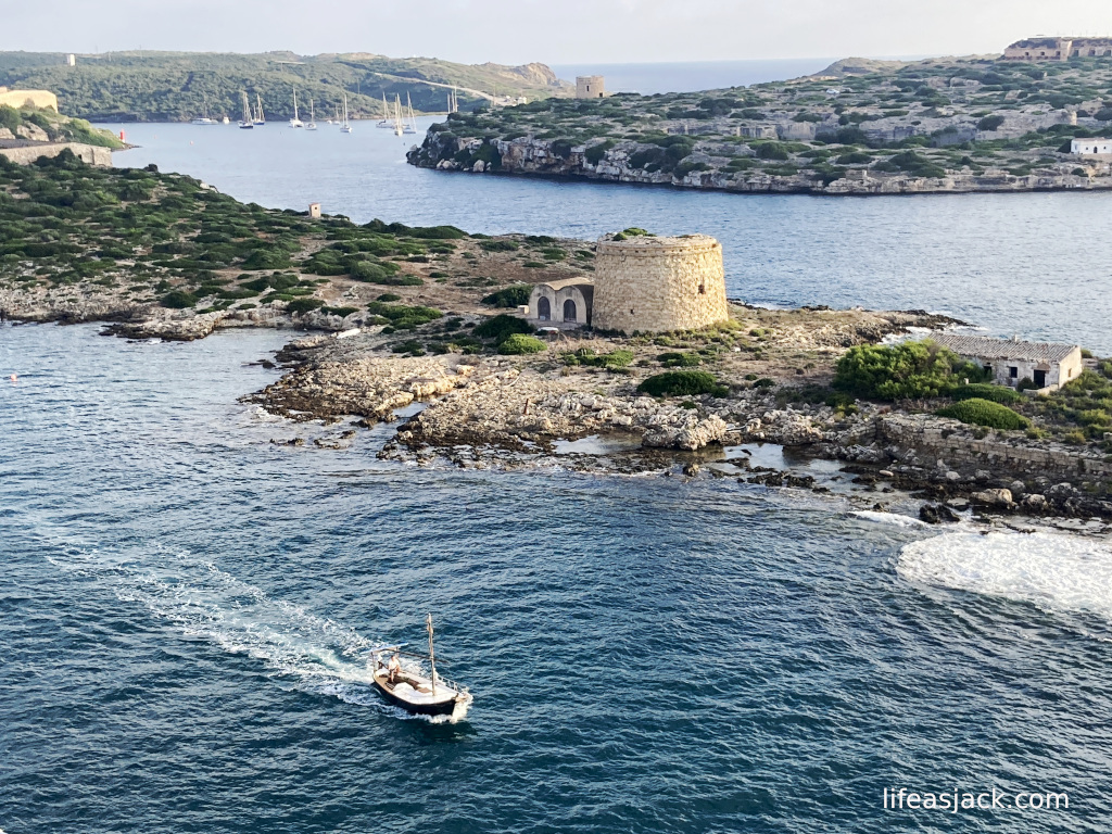 A fishing boat heads to sea past an ancient watch tower